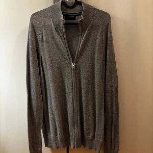 Grå kofta med dragkedja Bruun & Stengade - Snygg grå kofta från Bruun & Stengade i storlek L. Koftan har hel dragkedja framtill, ribbad krage och muddar. Perfekt för lager-på-lager och enkel att matcha med andra plagg. Mjuk och skön känsla, passar till många olika stilar. Knappt använd då jag har en del liknande tröjor. Hör av er vid intresse eller fler bilder!☀️