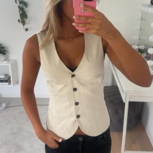 Beige väst med knappar - beige väst med djup v-ringning och svarta knappar framtill med en figurnära passform💕