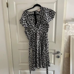Svartvit blommig klänning - Supersöt svartvit  klänning från Chica London med blommigt mönster. Endast använd en gång! Storleken är XL, men skulle vilja säga att den passar hos mindre storlekar med tanke på att den har inbyggt ”skärp” som du kan knyta åt på baksidan💕