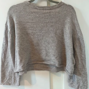 Beige croppad stickad tröja - Säljer en beige croppad stickad tröja med lång ärm. Perfekt för lager-på-lager och enkel att matcha med olika outfits. Tröjan har en avslappnad passform och ribbad kant vid halsen.