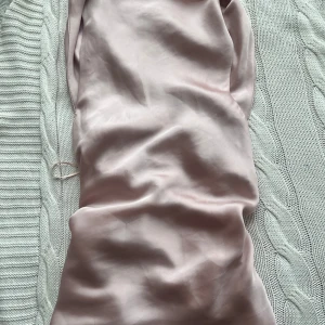 Ljusrosa satinklänning - Säljer en elegant ljusrosa klänning i satin med mjuk glansig yta. Klänningen har en slät design utan synliga mönster eller detaljer och känns riktigt lyxig. Perfekt för dig som gillar en stilren look.
