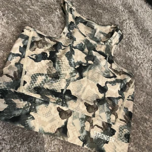 Camouflage sport-bh från Stronger - Sport-bh från Stronger i camouflage-mönster i beige, grått och grönt. Modellen är croppad och har brottarrygg. Perfekt för träning och tillverkad i polyester och elastan. Helt ny aldrig andvänd
