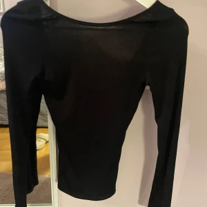 Svart topp med djup ringning från Nelly - Säljer en svart långärmad topp från Nelly med djup rund ringning. Toppen är tight och har en stilren, enkel design som passar perfekt till många olika outfits.