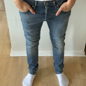 Blå slim fit jeans - Säljer ett par blå slim fit Jack&Jones jeans med lätt slitna detaljer och klassisk femficksdesign. Jeansen har normal midja och raka ben, tillverkade i denim med stretch för extra komfort. Perfekta för en avslappnad stil. Skick 9/10. DM för frågor🙌