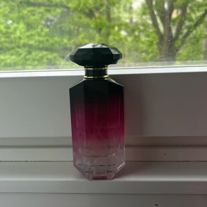 Victoria's Secret parfym  - Säljer en parfym från Victoria's Secret i en elegant flaska med svart facettslipat lock. Flaskan har en snygg färgövergång från svart upptill till rosa och genomskinlig nedtill. Guldiga detaljer runt halsen ger en lyxig känsla. det finns nästan halva kvar,