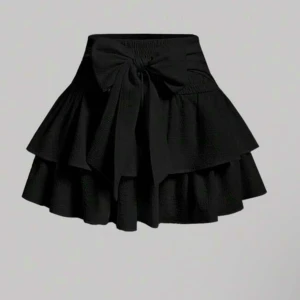 Svart volangkjol med rosett - Supersöt svart kortkjol med dubbla volanger och en stor rosett framtill i midjan. Inte använd!