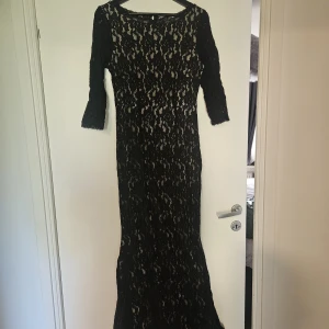 Svart långklänning i spets från Bodyflirt - Säljer en elegant svart långklänning från Bodyflirt med vackert spetsmönster och trekvartsärm. Klänningen har öppen rygg och figurnära passform, perfekt för festliga tillfällen. Klassisk och stilren design.