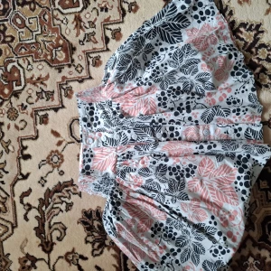 Blommiga shorts med resårmidja - Säljer ett par luftiga shorts med blommigt mönster i svart, rosa och vitt. Shortsen har bred resår i midjan och är tillverkade i ett tunt, mjukt tyg som passar perfekt för varma dagar.