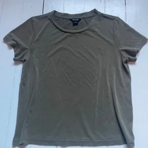 Olivgrön t-shirt från Monki - En basic olivgrön t-shirt från Monki med rund halsringning och korta ärmar. Tillverkad i mjukt material som känns skönt mot huden. Perfekt att matcha med jeans eller kjol för en enkel och stilren look.