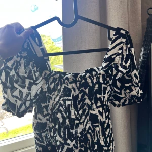 Svartvit mönstrad klänning från Monteau Los Angeles - Säljer en svartvit blus/top från Monteau Los Angeles med abstrakt mönster. Den har korta puffärmar och smockad överdel för en bekväm passform. 