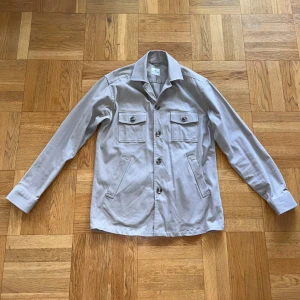 Beige overshirt från John Henric - Säljer nu en stilren beige overshirt från John Henric som är enkel att matcha med olika outfits. Har bara haft på mig den ett fåtal gånger så den är i bra skick. Hör av dig om du har några frågor.
