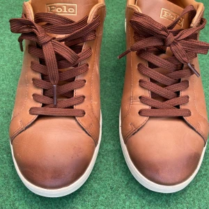 Bruna sneakers från Polo Ralph Lauren - Snygga bruna sneakers från Polo Ralph Lauren med klassisk design. Skorna har rund tå, platt vit sula och bruna snören. Tillverkade i skinn med diskret Polo-logga på sidan och insidan. Perfekta för en stilren vardagslook.