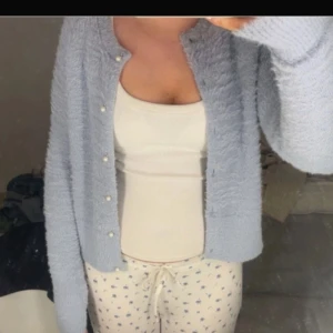 Ljusblå kofta med pärlknappar - Mysig ljusblå kofta med pärlknappar framtill. Koftan har lång ärm och är gjord i ett fluffigt, stickat material. Perfekt att slänga över en topp för en avslappnad look.