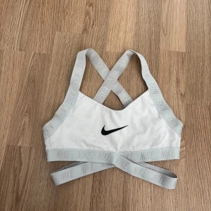 Vit sport-bh Nike - Säljer en vit sport-bh från Nike med korsade band fram och bak. Perfekt för träning och ger bra stöd. Pris 100kr. Storlek XS