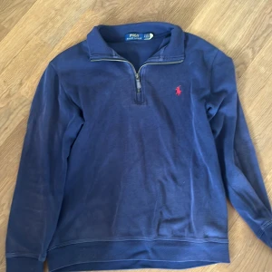 Halfzip Ralph lauren STEAL‼️ - Mörkblå långärmad tröja från Polo Ralph Lauren med halv dragkedja och röd broderad logga på bröstet. Klassisk krage och ribbade muddar. Perfekt för en stilren och avslappnad look. Storlek S