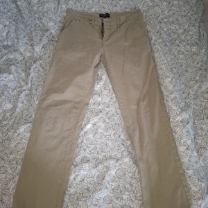 Beiga chinos från Hampton Republic - Säljer ett par stilrena beiga chinos från Hampton Republic i slim fit-modell. Byxorna har klassisk design med fickor fram och bak samt knapp och dragkedja i midjan. Perfekta för en clean och enkel look.