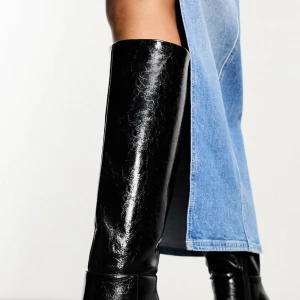 Svarta höga stövlar med klack - Säljer ett par svarta höga stövlar i glansigt skinnimitation. Stövlarna har spetsig tå och smal klack, vilket ger en snygg och trendig look, Anvlnda  bara två gånger   Perfekta att styla med kjol eller klänning för en cool outfit. Storlek 40 men mer som 39