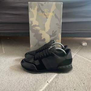 Valentino rockrunners - Säljer ett par svarta Valentino Garavani sneakers med matta och blanka partier samt diskret camouflage-mönster. Skorna har snörning och rund tå, och levereras med originalkartong i camouflage-design.