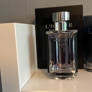 L'Homme Prada Pour Homme Eau de Toilette - Elegant parfymflaska från Prada med silvrig kork och transparent glas. Doften är maskulin och modern, perfekt för dig som gillar stilrena och exklusiva parfymer. Flaskan har raka linjer och en lyxig känsla.