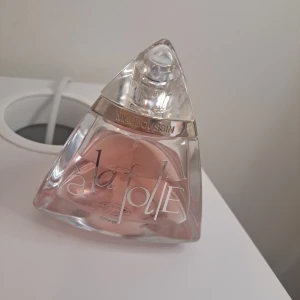 Parfym Mauboussin à la folie EDP  - Elegant parfym från Mauboussin med en unik, triangulär flaska i glas. Innehållet är en vacker rosa nyans som ger en känsla av lyx och romantik. Perfekt för den som vill ha en doft som sticker ut. Använt 1 spray 1 gång bara. 