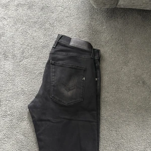 Svarta jeansbyxor från Replay - Säljer ett par svarta jeansbyxor från Replay med klassisk femficksdesign och diskreta Replay-detaljer. Byxorna har normal passform och är tillverkade i ett mjukt bomullsmaterial med lite stretch. Midjan är midwaist och storleken är W31 L34.
