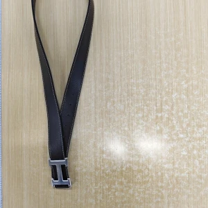 Svart skärp med silverfärgat H-spänne - Säljer ett svart bälte i skinn med ett stort, silverfärgat H-format spänne. Bältet har vita sömmar längs kanterna och en klassisk design som passar till många olika stilar.