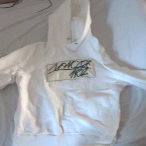 Vit hoodie från Moncler med tryck - Säljer en vit hoodie från Moncler med stor huva och tryckt text på bröstet. Tröjan har en broderad Moncler-logga på ärmen och klassisk känguruficka framtill. Perfekt för dig som gillar streetwear och exklusiva märken.