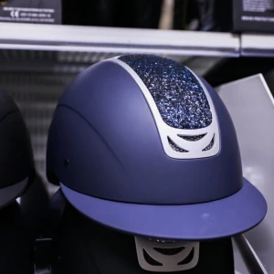 Blå ridhjälm med glittrig detalj - Snygg blå ridhjälm med glittrig panel framtill och silverfärgade detaljer. Hjälmen har en klassisk form med skärm och är perfekt för dig som vill sticka ut i stallet. Den är sparsamt använd och i bra skick! 
