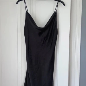 Svart satinklänning med smala axelband - Säljer en supersöt svart satinklänning med smala justerbara axelband och cowlneck-ringning från Gina Tricot. Klänningen är satinliknande material och är kort i modellen. Perfekt för dig som gillar minimalistisk och stilren design! Aldrig använd av mig, köpt på plick tidigare men oanvänd då också. Säljer pga brist av användning 🩷