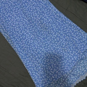 Blå blommig klänning från SHEIN - Söt blå klänning från SHEIN med små vita blommor över hela tyget. Klänningen är i en lätt och luftig polyester, perfekt för varmare dagar. Den har en klassisk passform och är helfodrad nertill med spetskant.