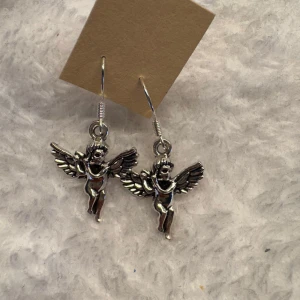 Silverfärgade ängelörhängen - Säljer ett par unika örhängen i silverfärg med detaljerade änglar som motiv. Perfekta för dig som vill ha något speciellt och iögonfallande till din stil. Hängande modell med krok. Krokarna är i sterling silver