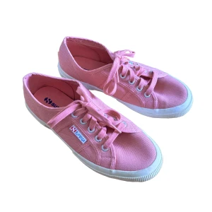 Rosa sneakers från Superga - Säljer ett par klassiska rosa sneakers från Superga med vit sula och snörning. Skorna har en låg modell och är tillverkade i canvas med Superga-logga på sidan.