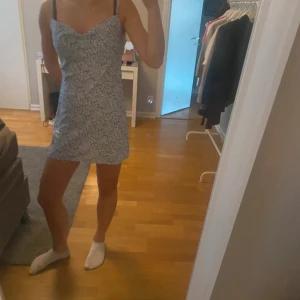 Ljusblå blommig kortklänning - Söt ljusblå kortklänning med smala axelband och blommigt mönster. Klänningen har en feminin passform och lätt v-ringning framtill. Perfekt för varma dagar och somriga tillfällen.