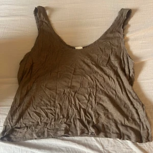 Brun ribbad linnetopp från H&M - Säljer en brun ribbad linnetopp från H&M i storlek XL. Toppen har en djup rundad halsringning och är ärmlös, perfekt för varma dagar eller som lager under andra plagg.