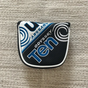Svart och vit Odyssey Ten putter headcover - Säljer ett Odyssey Ten headcover för putter, svart med vita och blå detaljer. Utsidan är i syntetmaterial med broderad logga och text, insidan är fodrad med mjuk blå plysch. Magnetlås för enkel öppning och stängning.