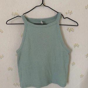  linne - Säljer en ljusgrön ribbad linnetopp från ONLY. Toppen har hög halsringning och är ärmlös med croppad passform. Perfekt för varma dagar och enkel att matcha med olika outfits.