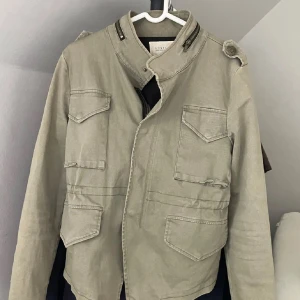 Filed Jacket  - Snygg beige jacka från Costes med coola dragkedjor vid kragen och axelremmar. Fyra fickor framtill och ståkrage ger en stilren look. Perfekt för dig som gillar en lite tuffare stil och en snygg till sommaren också . Den är i St M men skulle säga att den passar mer för dom som har St S för den har krympt lite😃