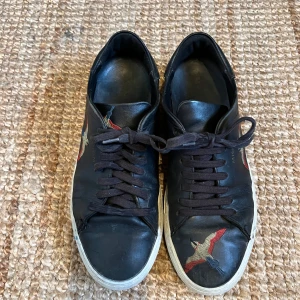 Axel Arigato svarta sneakers stl 43 - Svarta sneakers med vita sulor och broderade fåglar i rött, blått och beige på sidorna och framtill. 
