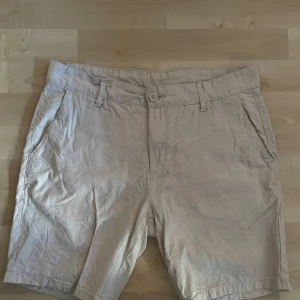 Beige shorts i linne/bomullsblandning - Snygga beige shorts från Cubus i en skön blandning av linne och bomull. Klassisk passform med fickor fram och bak, bälteshällor och knappstängning. Perfekta för varma dagar.
