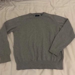 Grå stickad tröja från GANT - Säljer en klassisk grå stickad tröja från GANT med rund halsringning och diskret broderad logga på bröstet. Slim fit storlek 158/164 13 -14 år 