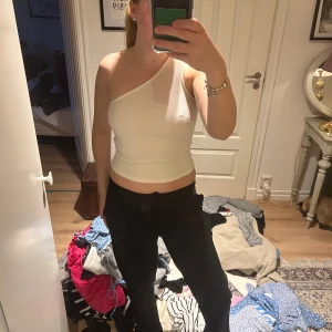 Vit one shoulder topp - Säljer en vit ribbad one shoulder topp med tight passform. Toppen är ärmlös och har en asymmetrisk design med en axel. Perfekt för att skapa en trendig och stilren look.