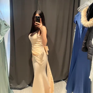 Champagnefärgad långklänning med slits och omlott - Säljer en elegant champagnefärgad långklänning med omlottdetalj och slits framtill. Klänningen har smickrande passform och markerad midja med knytband. Perfekt för bal eller fest. Köpt från Sasha butiken i Södertälje, Nypris 3800kr. 