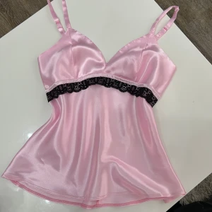 Rosa satin pyjamas med spets - Snygga ljusrosa pyjamas  i satin med elastisk midja och svart spetsdetalj längs bensluten. Perfekta för en mysig hemmakväll eller sommarens varma nätter. Mått: Byst- 85 cm. Höft- 90 cm 