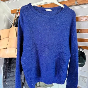 Blå stickad tröja från American Vintage - Mysig blå stickad tröja från American Vintage med rund halsringning och långa ärmar. Perfekt för lager-på-lager och enkel att styla till olika outfits. Tröjan har en klassisk, avslappnad passform.