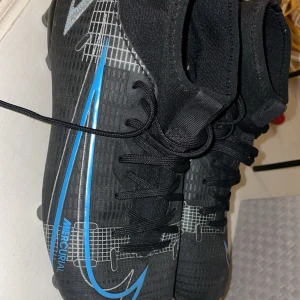 Nike Mercurial fotbollsskor - Säljer ett par svarta Nike Mercurial Superfly VIII Academy AG Football Boots! med blå och silver detaljer. Skorna har snörning, högre skaft och mönstrad ovandel. Perfekta för dig som vill ha stilrena och snabba skor på planen. Bara använda på 2 träningars de var för små för mig!🔥🔥