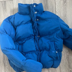 Pufferjacka - Säljer en blå kortare pufferjacka från Newyorker i storlek S. Jackan har hög krage, dragkedja och tryckknappar framtill samt två fickor med lock. Perfekt för kyligare dagar.🤍