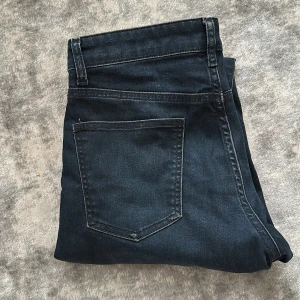 Mörkblå jeansbyxor från J.Lindeberg - Säljer ett par mörkblå jeansbyxor från J.Lindeberg med klassisk femficksdesign och raka ben. Byxorna har normal passform och är tillverkade i ett mjukt jeansmaterial. Storlek w30 l34. Pris kan diskuteras!