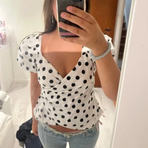 Vit omlottblus med svarta prickar - Säljer en vit omlottblus med svarta prickar och puffiga korta ärmar. Blusen har djup v-ringning och markerad midja som ger en snygg siluett. Perfekt för dig som gillar trendiga och lekfulla plagg. Storlek L men sitter som S💕