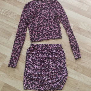 Svart och rosa blommigt set - Svart och rosa blommig kjol och tröja set! En svart mesh genomskinlig rosa blommig långärmad tröja tillsammans med en svart rosa blommig tight schrunchad kjol. Passar perfekt till en sommarkväll. Storlek: Kjol=XS+etikett Tröja= Ingen etikett men ca XXS/XS. Köpt ifrån H&M enskilt. Använd bara ett par antal gånger, mycket god skick. 