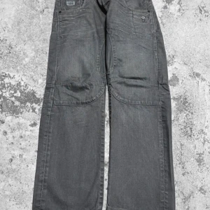 Gråa wide jeansbyxor  - Säljer ett par gråa jeansbyxor från Jack and jones med bred passform och stora bakfickor. Byxorna har knappar och dragkedja framtill samt detaljerade sömmar över benen. Perfekta för dig som gillar en avslappnad och trendig stil. Midja:88cm   Ben: 20 cm   Totallängd: 100 cm